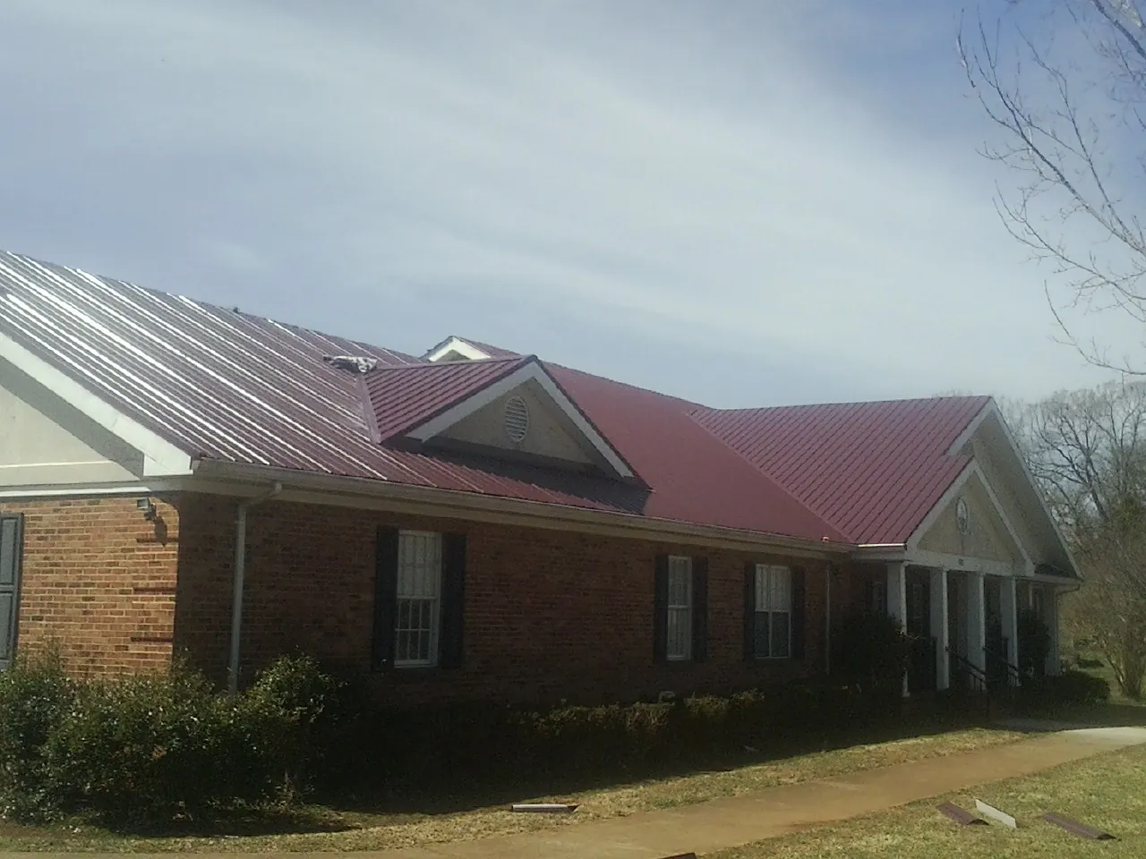 Red metal roof with gabled entries on a long brick building, from a Hail Damage Roof Repair job in Victor