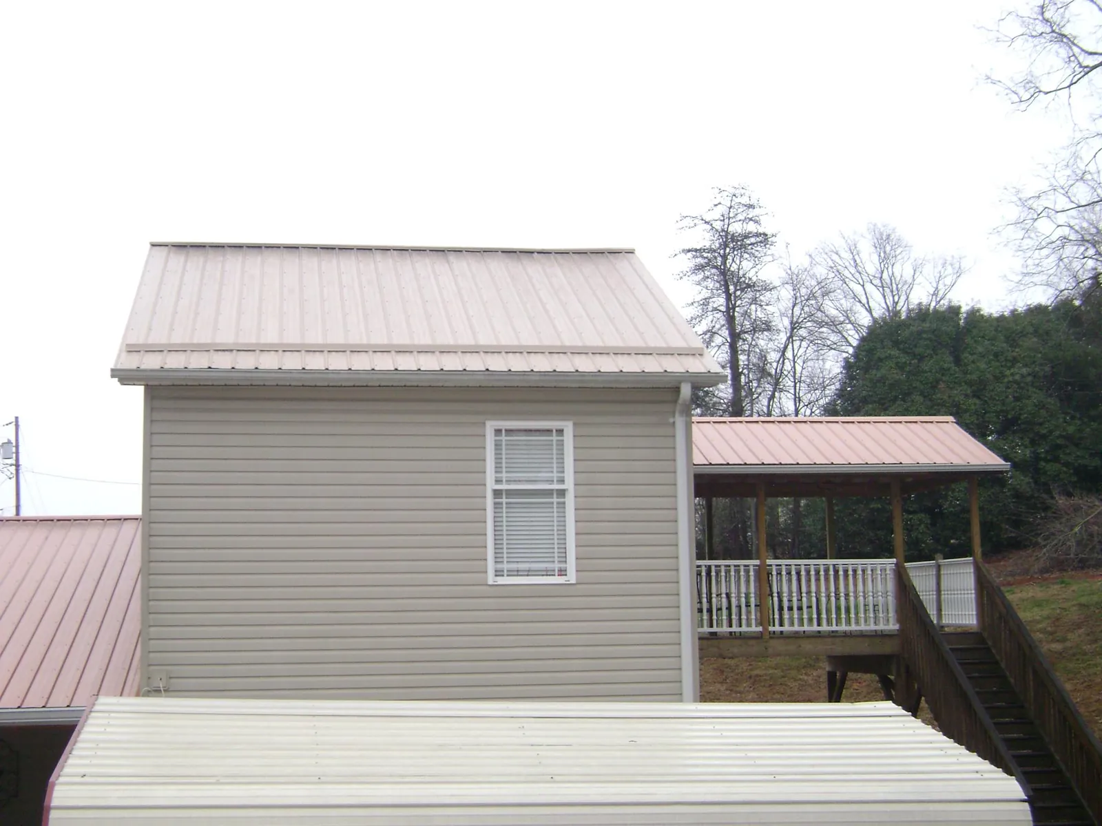 Tan metal roofs on a two story addition and attached porch, from a Roof Replacement job in Victor