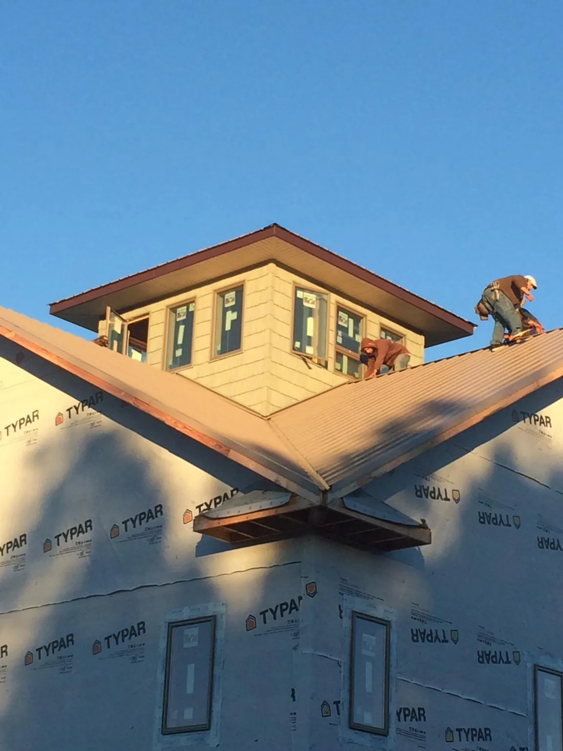 Roofers working around a rooftop cupola on a new metal roof at sunset — Roof Waterproofing in Victor by Roofing Brothers
